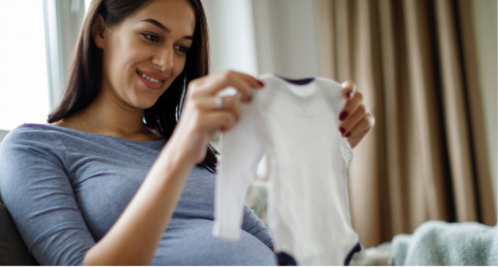 image of a pregnant woman holding up a onesie
