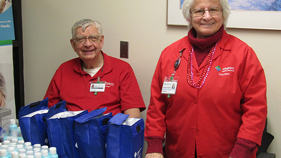 two AHN volunteers in their red coats standing at a table with water bottles and other supplies