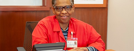 AHN volunteer in her red coat sitting at a desk and smiling at the camera