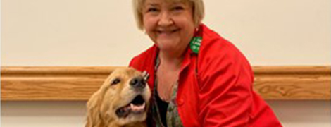AHN volunteer in her red coat smiling and petting her therapy dog