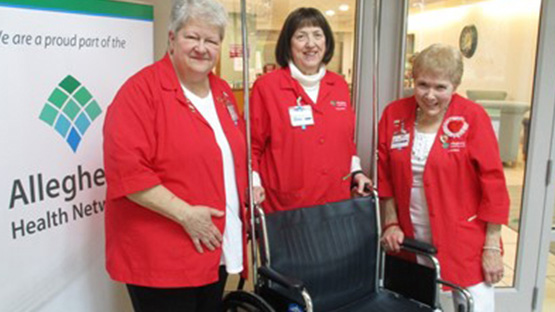 three AHN volunteers standing around a wheelchair in their red coats