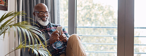 man sitting in comfortable chair smiling as he downloads the MyChart app on his smartphone