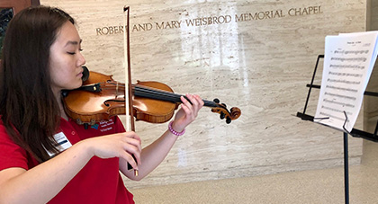 AHN volunteer in her red volunteer shirt playing her violin