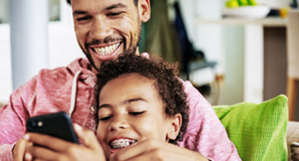 young boy with braces smiling as his father makes an appointment on his phone
