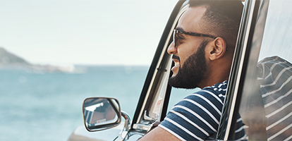 Man wearing sunglasses smiling as he views the beach from his car window