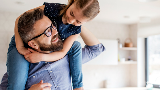 man smiling as he holds his daughter on his shoulders