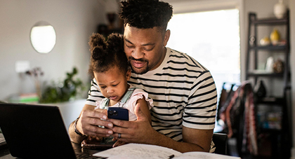 father holding his young doctor and checking an app on his phone