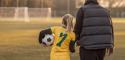 parent holding hands with their child and walking across a soccer field