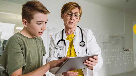 physician going over information on a tablet with a teenage patient