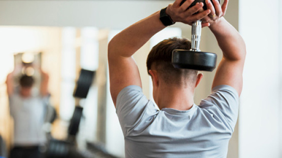 student athlete lifting a dumbbell behind their head in a weight room