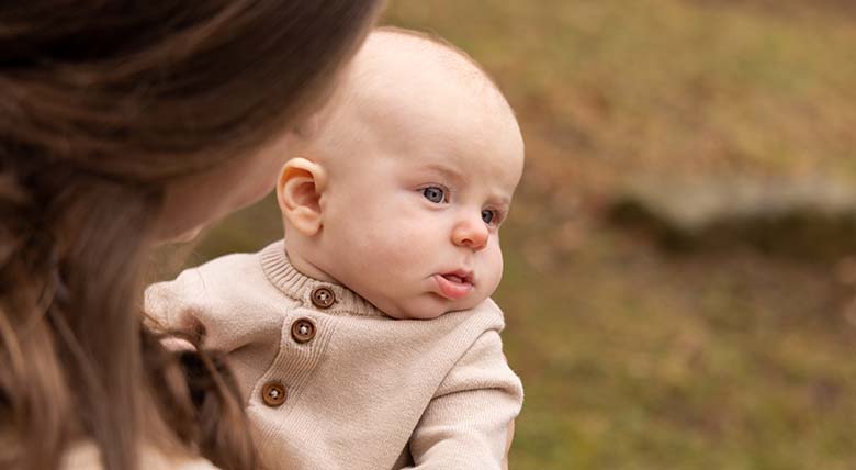 Photo taken from behind a mother's shoulder as she holds her baby outdoors
