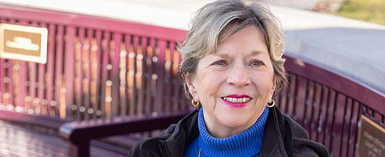 Woman smiling at the camera as her photo is taken on a bench outside